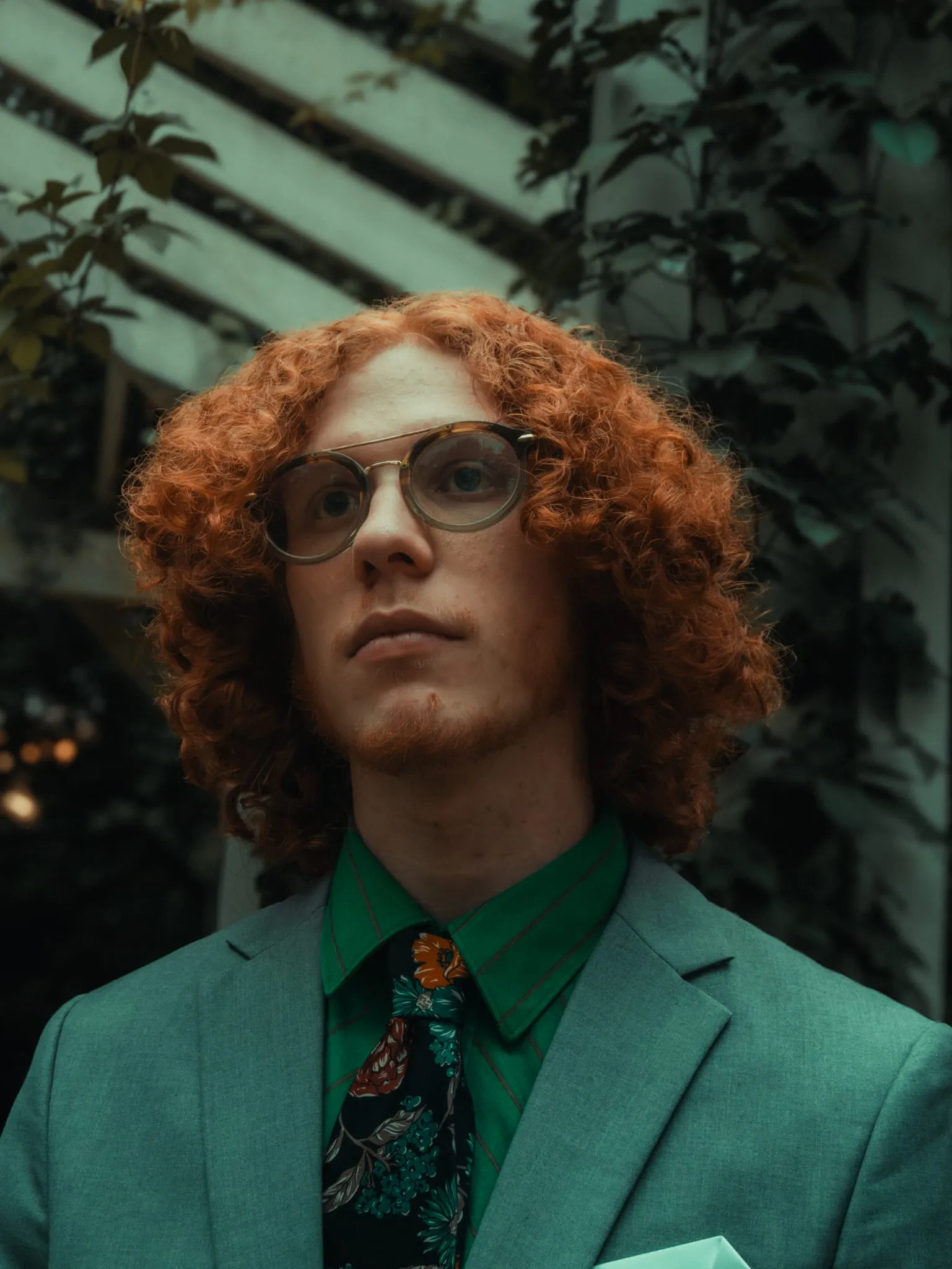 Styled editorial fashion portrait in a green suit against an ivy-covered wall