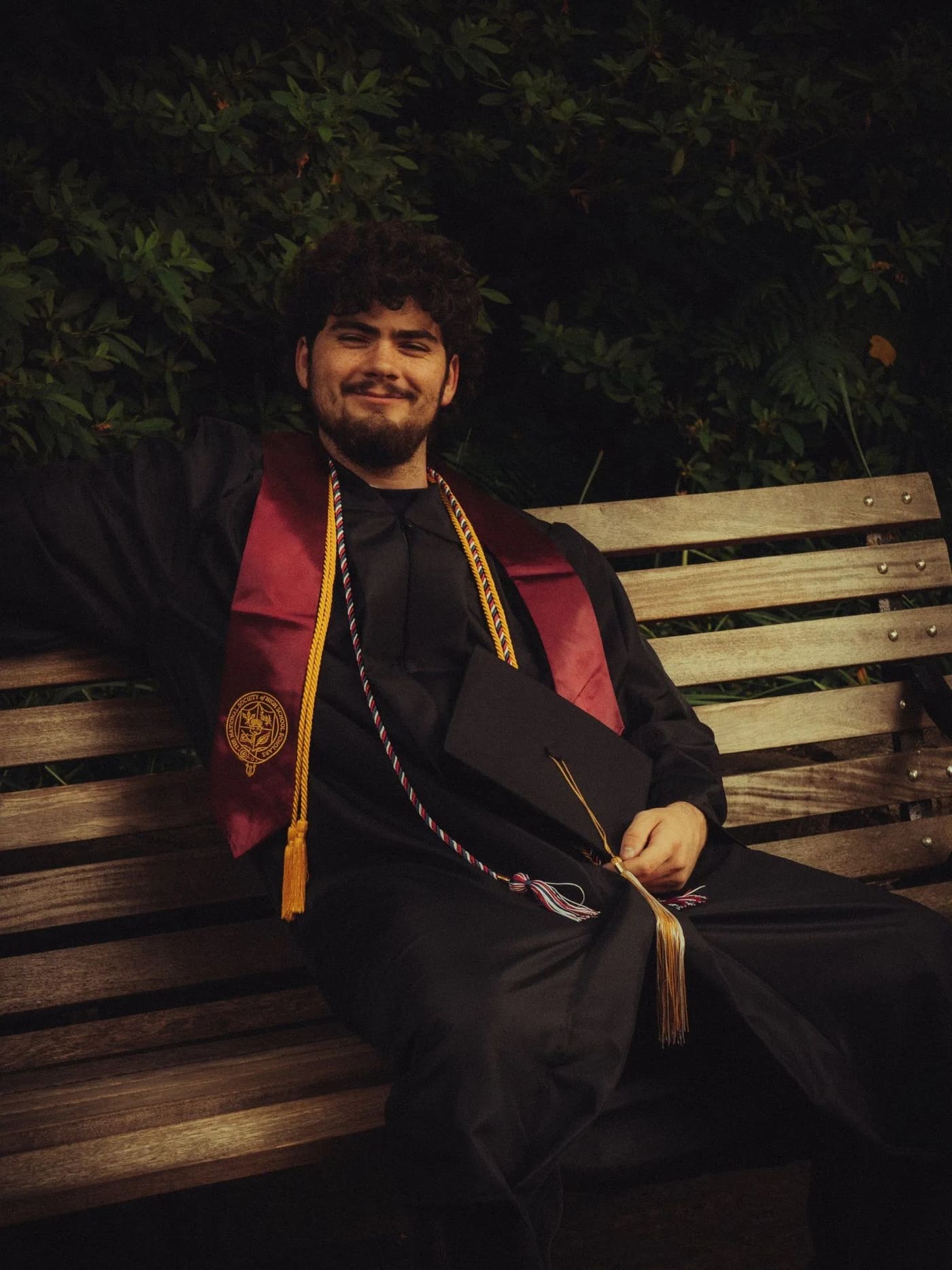 Graduate in cap and gown seated on a wooden bench